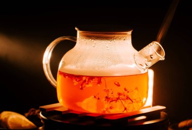 Black tea brewing with flowers and steam in a warm setting during evening hours