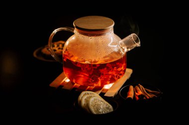 Brewing black tea with spices and lemon on a wooden tray in a dimly lit setting