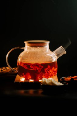 Steam rises from a glass teapot filled with black tea on a wooden coaster