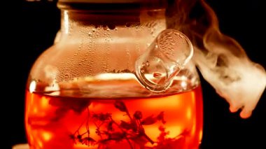 Brewing vibrant black tea with herbs and steam in a glass pot at home