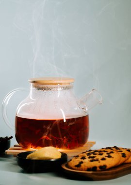 Warm tea with steam rising beside cookies and butter on a wooden table