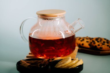 Warm tea in a clear pot with lemon slices and cookies on a table in a cozy setting