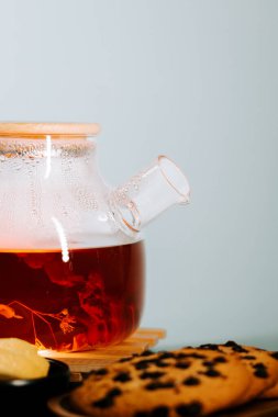 Steaming tea kettle with a warm beverage alongside cookies and lemon slice