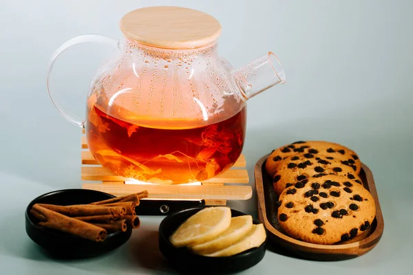 Tea brewing in a glass pot with lemon slices and chocolate chip cookies on wooden plates