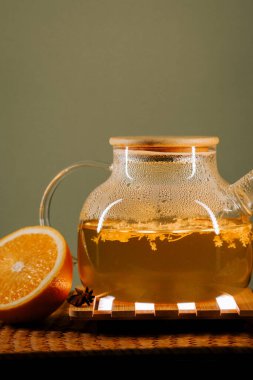Warm green tea with orange on a wooden tray beside a misty glass teapot