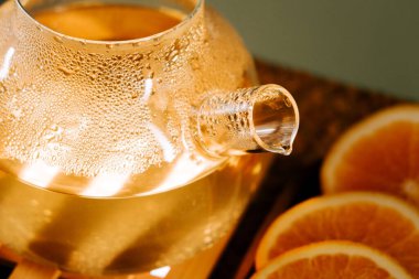 Refreshing green tea steeping in a clear teapot with orange slices nearby