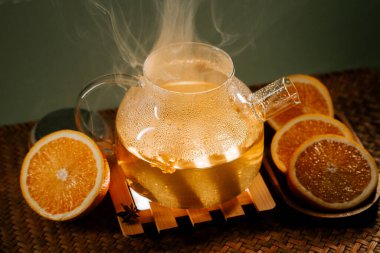 Delicious green tea with orange slices steaming on a wooden tray