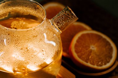 Delicate teapot with green tea and fresh orange slices on a wooden table