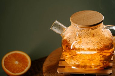 Warm green tea kettle steaming beside fresh orange on a wooden table in calming setting