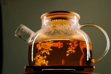Warm green tea steeping in a clear glass kettle on a wooden coaster