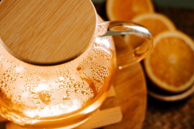 Warm green tea steaming in a glass kettle with orange slices nearby