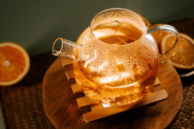 Scented green tea brewing in a clear glass teapot with orange slices on a wooden tray