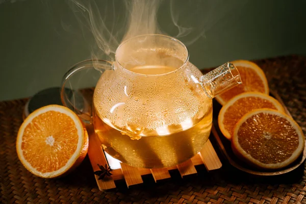 Delicious green tea with orange slices steaming on a wooden tray