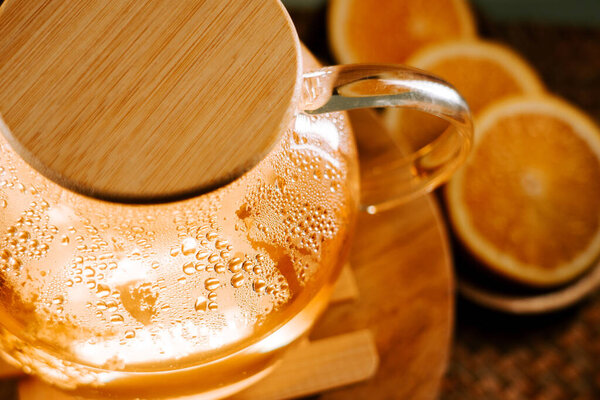 Warm green tea steaming in a glass kettle with orange slices nearby