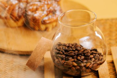 Freshly roasted coffee beans in a glass jar beside delicious pastries on a wooden surface