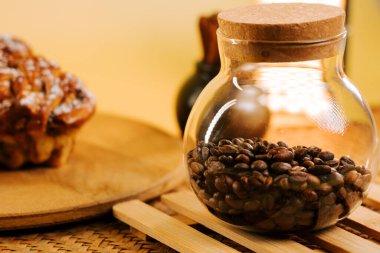Coffee beans in a glass jar next to a sweet pastry on a wooden tray
