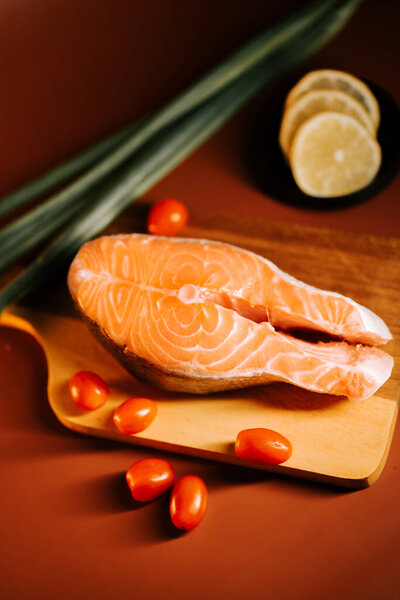 Fresh salmon steak with cherry tomatoes and lemon slices on a wooden cutting board