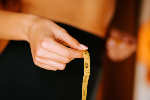 Измерение размера талии с помощью рулетки, фокусируясь на здоровье и фитнес целей в домашних условиях