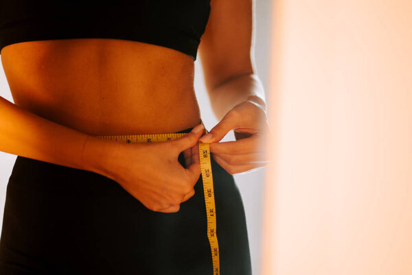 Проверка талии измерений во время фитнес-поездки дома в мягком утреннем свете