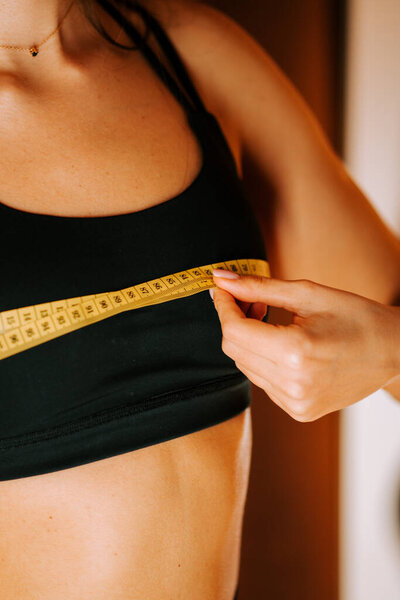 Женщина измеряет талию рулеткой в ярком помещении днем