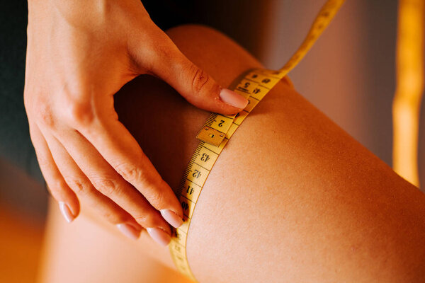 Измерение бедра желтой измерительной лентой в теплой внутренней обстановке