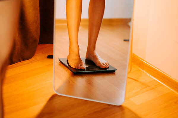 Person weighing themselves in a home setting with a mirror in the background