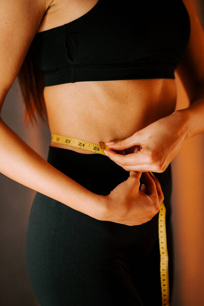 Женщина измеряет талию с помощью рулетки дома во время тренировки при теплом освещении
