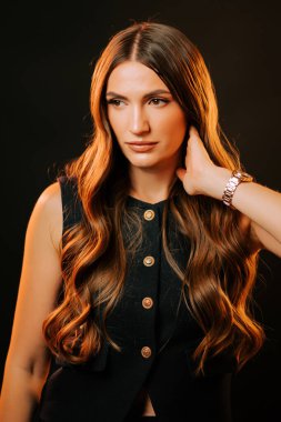 Uzun saçlı genç bir kadın siyah arka planda poz veriyor, zarafet ve tarz sergiliyor.