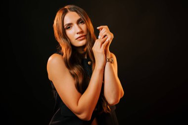 Koyu bir zemine karşı poz veren zarif bir kadın uzun saçlarını ve zarif hareketlerini sergiliyor.