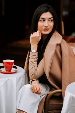 Kadın zarif giyinmiş, rahat görünen, tuhaf bir İtalyan kafesinde kahvesini yudumluyor.