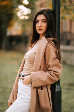 Sonbaharda bir parkta direğe yaslanmış şık kıyafetli genç bir kadın.