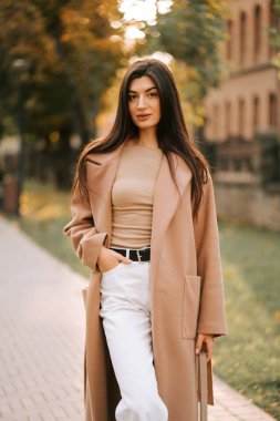 Şık ceketli bir kadın sonbahar öğleden sonrasında şehir yolunda yürüyor.