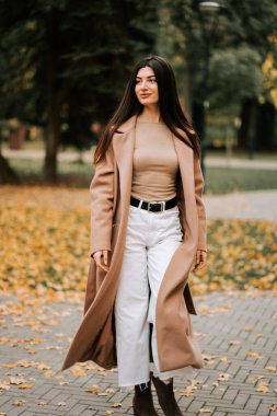 Sonbaharda, yerde renkli yapraklarla parkta yürüyen zarif bir kadın.