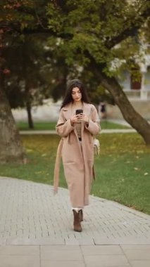 Serin bir sonbahar gününde telefon kullanarak parkta yürüyen bir kadın.