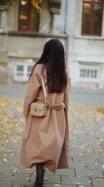 Sonbahar parkında düşen yapraklar ve şık bir ceketle yürüyen bir kadın.