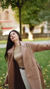 Şık ceketli bir kadın sonbahar öğleden sonra yürüyüşü sırasında şehir parkını geziyor.