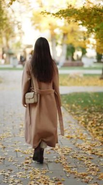 Sarı yapraklar ve ağaçlarla çevrili sonbahar parkında yürüyen bir kadın.