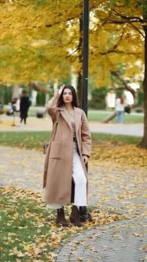 Genç kadın renkli yapraklarla çevrili parkta sonbahar gezintisinden hoşlanıyor.