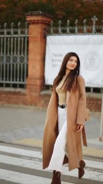 Genç bir kadın şehir caddesinde şık bir kıyafetle güneşli bir günün tadını çıkarıyor.