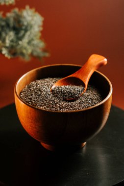 Koyu bir yüzeyde kepçeyle ahşap bir kasede kavrulmuş chia tohumları.