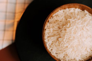 Uzun tahıllı beyaz pirinç, ahşap kasede, koyu yüzeyde duruyor.