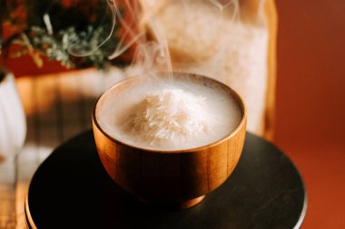 Sıcak bir mutfak masasında, ahşap bir kasede servis edilen buğulanmış beyaz pirinç.