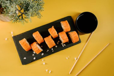 Taze suşi ruloları siyah bir tepside servis edilir. Çubuklar ve soslar güneşli bir masada.