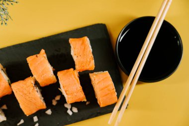 Taze suşi dürümleri. Sos ve yemek çubuklarıyla birlikte koyu bir tabakta.