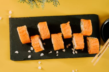 Siyah bir tabakta servis edilen lezzetli suşi dürümleri, parlak sarı bir arka plan.