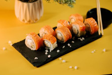 Taze suşi ruloları, parlak sarı arkaplanlı siyah bir levhada servis edilir.