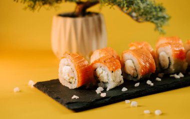 Suşi yuvarlakları, sarı arka planı ve bitkisi olan bir tabağa güzelce yerleştirilmiş.