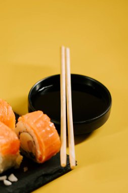 Somonlu suşi, soya sosu ve sarı arka planda çubuklar.