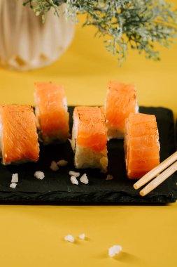 Taze somon suşisi ruloları, yemek çubukları ve sarı arka planla servis edilir.