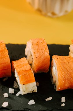 Siyah tahtada servis edilen lezzetli suşi dürümleri ve parlak sarı bir arka plan.